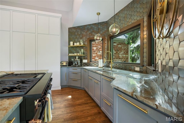 kitchen featuring gray cabinetry, gas range, a sink, light stone countertops, and open shelves