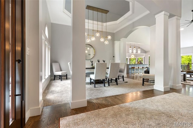 dining space with arched walkways, crown molding, wood finished floors, ornate columns, and a chandelier