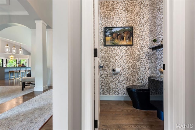 bathroom with baseboards, decorative columns, wood finished floors, wallpapered walls, and toilet