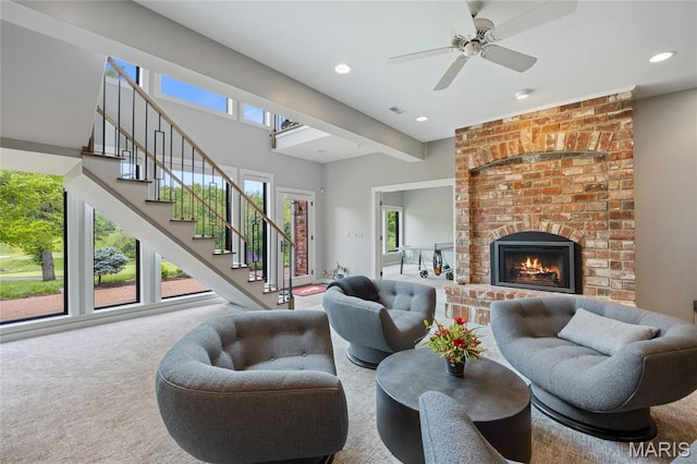 carpeted living room with stairs, a brick fireplace, plenty of natural light, recessed lighting, and ceiling fan