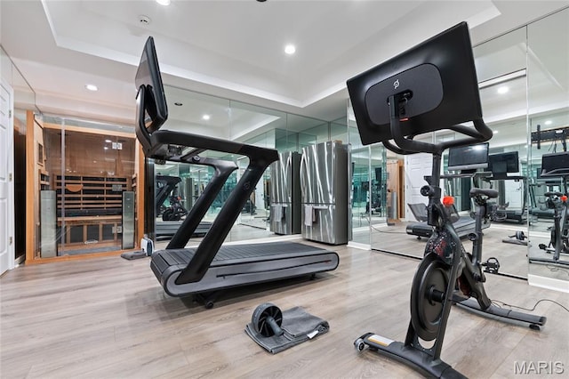 exercise room with a tray ceiling, wood finished floors, and recessed lighting