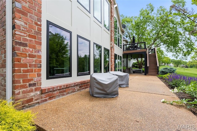 view of side of property featuring brick siding, stairway, a deck, and a patio area