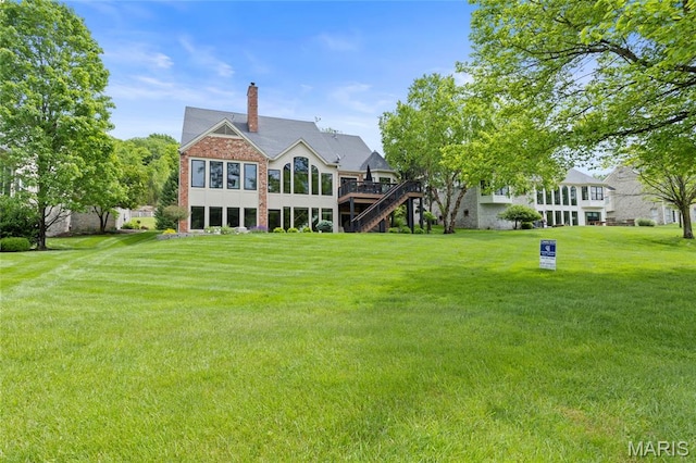 back of house featuring stairway, a yard, a wooden deck, a chimney, and brick siding