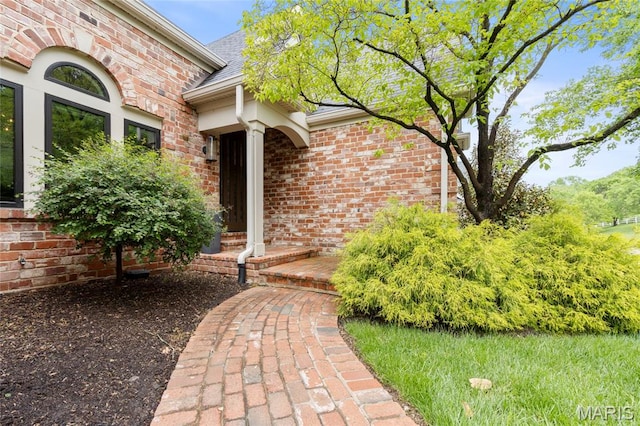 view of exterior entry with brick siding and a shingled roof