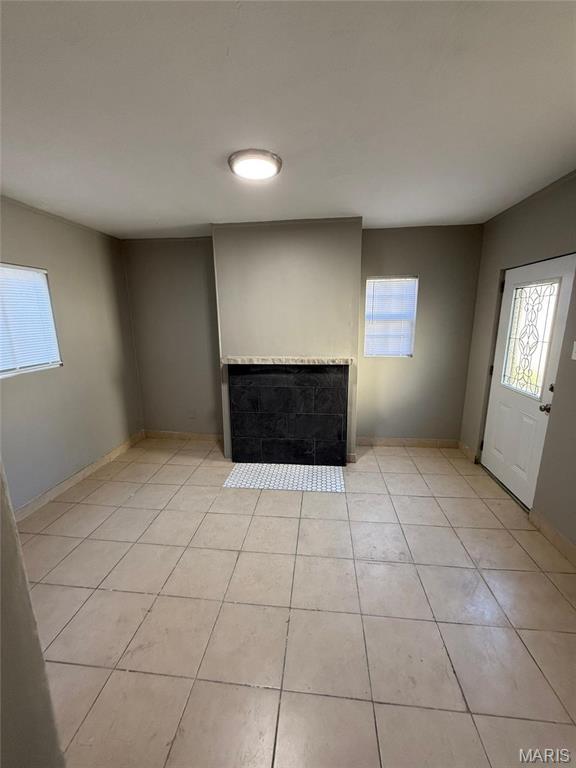 139 Euclid Ave, Saint Louis, MO 63119 - unfurnished living room with plenty of natural light, a tiled fireplace, light tile patterned floors, and baseboards