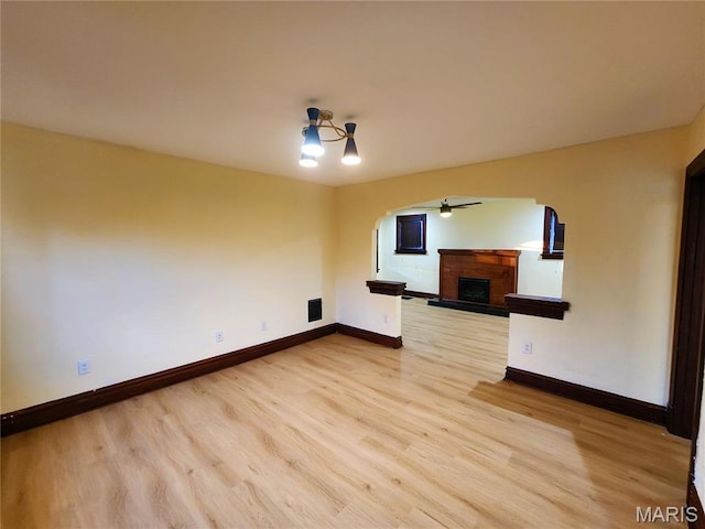 436 Hern Ave, Saint Louis, MO 63135 - spare room with a fireplace with raised hearth, arched walkways, light wood-style floors, and baseboards
