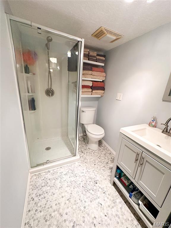 full bath featuring baseboards, toilet, a shower stall, vanity, and a textured ceiling