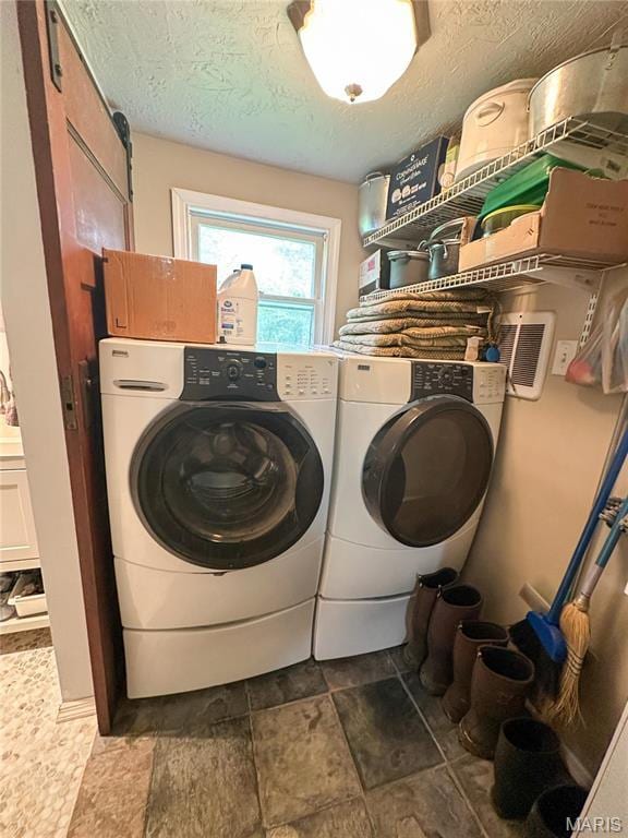 laundry room featuring washing machine and clothes dryer, stone finish floors, and a textured ceiling