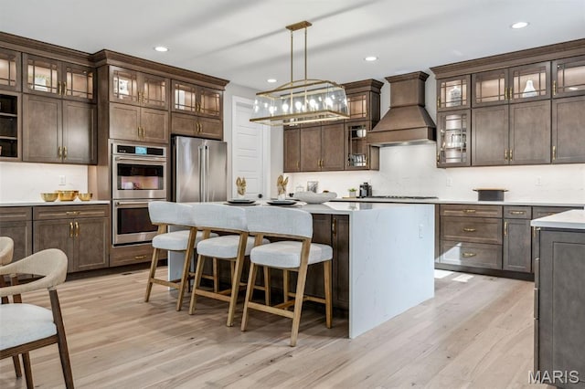 973 Tara Ct, Chesterfield, MO 63005 - kitchen featuring appliances with stainless steel finishes, premium range hood, dark brown cabinets, a center island, and light wood-style floors