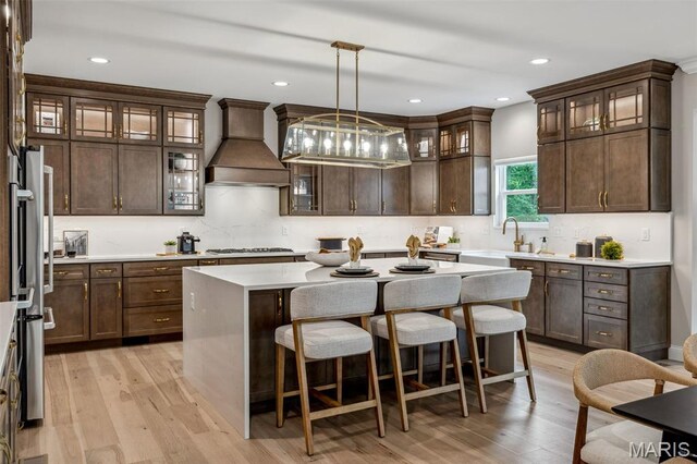 973 Tara Ct, Chesterfield, MO 63005 - kitchen featuring premium range hood, a breakfast bar area, stainless steel gas stovetop, light wood-style flooring, and dark brown cabinetry