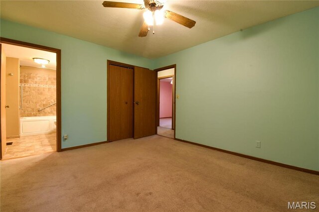 unfurnished bedroom with carpet flooring, baseboards, a closet, ensuite bath, and a ceiling fan
