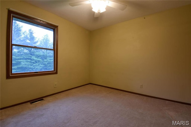 empty room with light colored carpet, a ceiling fan, and baseboards