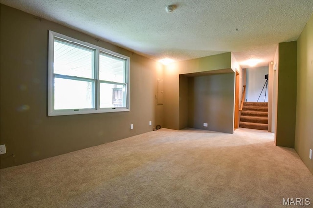 carpeted empty room with a textured ceiling, stairs, and a smoke detector