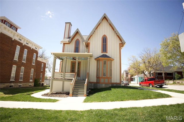 view of front of home featuring covered porch, board and batten siding, a chimney, and a front yard
