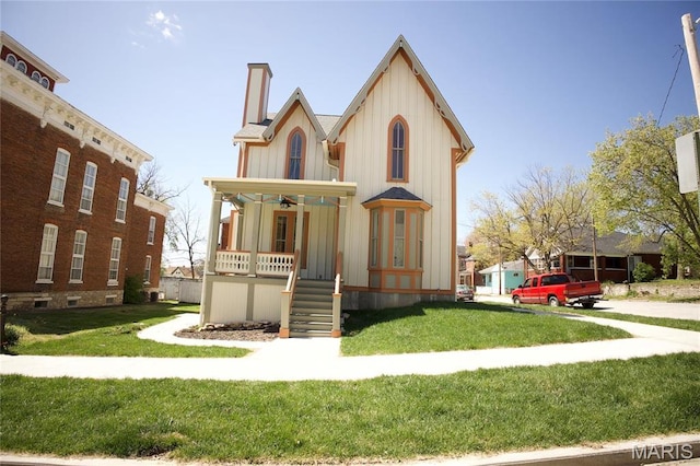 view of front of house featuring covered porch, board and batten siding, a chimney, and a front lawn