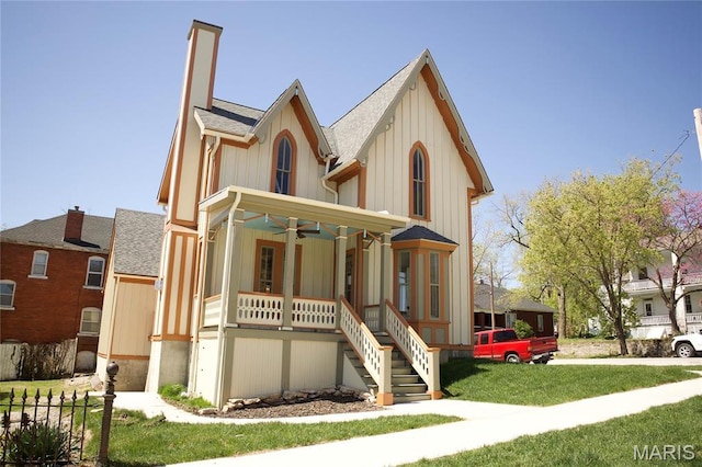 view of front of property with covered porch, a ceiling fan, stairs, a shingled roof, and a front lawn