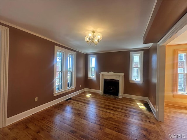 unfurnished living room featuring ornamental molding, baseboards, hardwood / wood-style flooring, a chandelier, and healthy amount of natural light