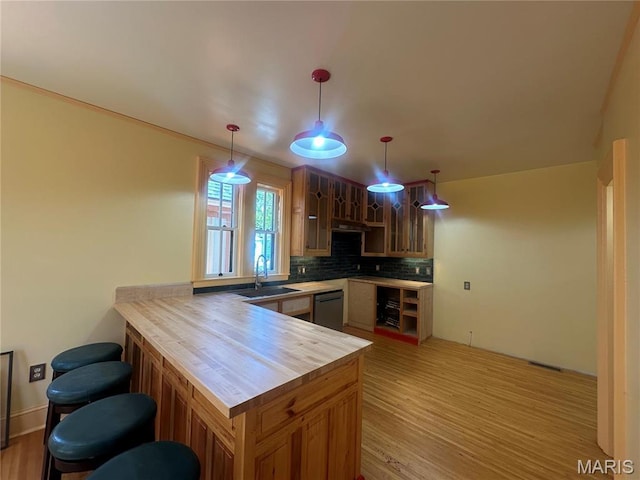 kitchen featuring dishwasher, a sink, backsplash, a peninsula, and light wood-style flooring