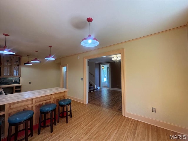kitchen featuring light wood finished floors, baseboards, a breakfast bar area, and decorative light fixtures