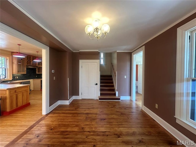 unfurnished dining area featuring a sink, stairway, a chandelier, plenty of natural light, and crown molding