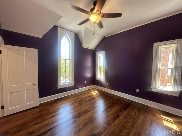 spare room featuring dark wood-type flooring, ceiling fan, baseboards, vaulted ceiling, and crown molding