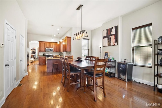 dining room featuring dark wood-style flooring, arched walkways, beverage cooler, and baseboards