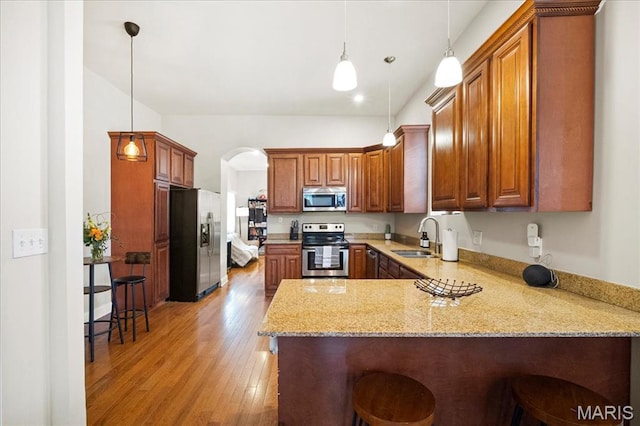 kitchen with appliances with stainless steel finishes, a sink, a peninsula, light stone counters, and light wood-style floors