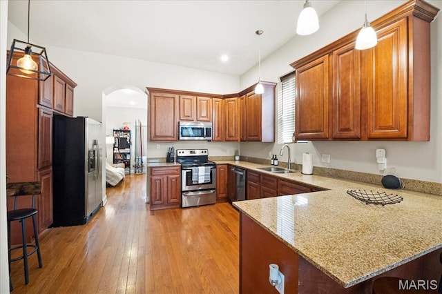 kitchen with stainless steel appliances, a peninsula, a sink, arched walkways, and brown cabinetry