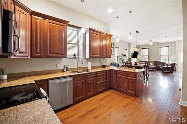 kitchen featuring appliances with stainless steel finishes, a sink, open floor plan, a peninsula, and pendant lighting