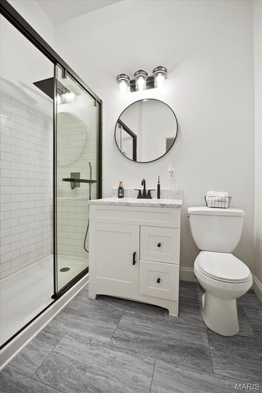 full bath featuring a stall shower, vanity, toilet, and baseboards