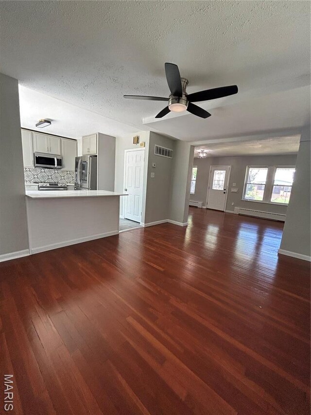 3604 Ridgedale Ave, Saint Louis, MO 63121 - unfurnished living room featuring dark wood-type flooring, a baseboard heating unit, a textured ceiling, a ceiling fan, and baseboards