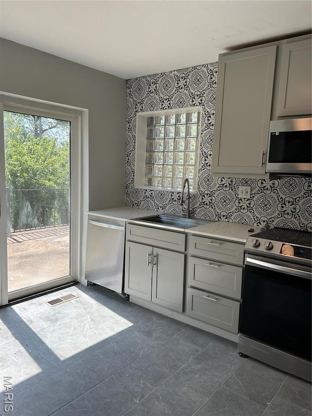 3604 Ridgedale Ave, Saint Louis, MO 63121 - kitchen with stainless steel appliances, a sink, gray cabinetry, and backsplash