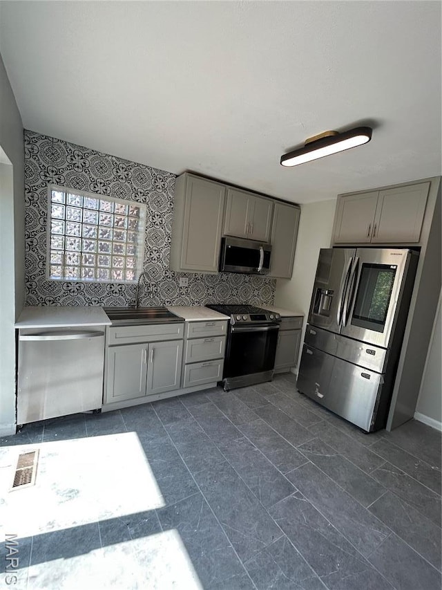 3604 Ridgedale Ave, Saint Louis, MO 63121 - kitchen with gray cabinets, appliances with stainless steel finishes, a sink, light countertops, and decorative backsplash