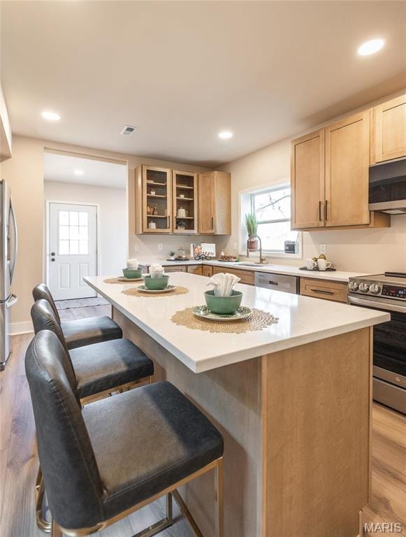 204 S 3rd St, De Soto, MO 63020 - kitchen featuring appliances with stainless steel finishes, a breakfast bar, glass insert cabinets, light countertops, and light wood-style floors