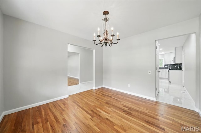 empty room featuring a chandelier, light wood-type flooring, and baseboards
