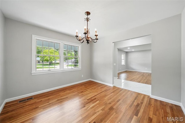 empty room with a chandelier, healthy amount of natural light, light wood-style flooring, and baseboards