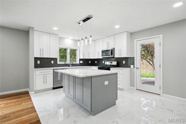 kitchen featuring appliances with stainless steel finishes, decorative backsplash, light marble finish flooring, baseboards, and a kitchen island