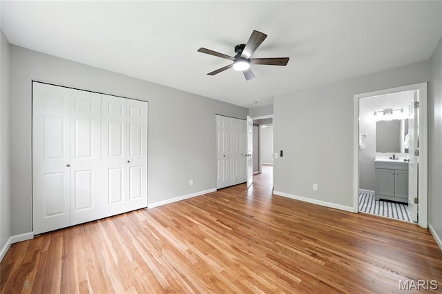 unfurnished bedroom featuring multiple closets, light wood-type flooring, baseboards, and a sink