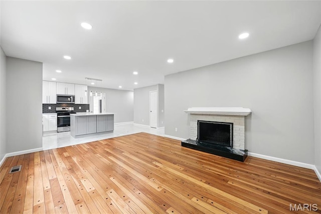 unfurnished living room with light wood-type flooring, baseboards, a brick fireplace, and recessed lighting