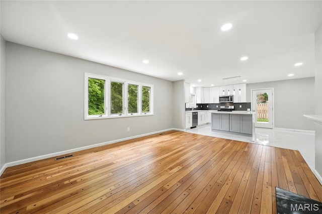 unfurnished living room featuring light wood-type flooring, baseboards, healthy amount of natural light, and recessed lighting
