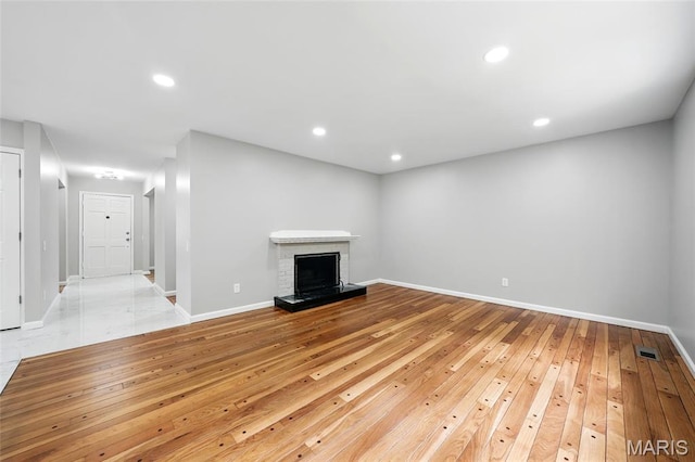unfurnished living room with hardwood / wood-style flooring, baseboards, recessed lighting, and a brick fireplace