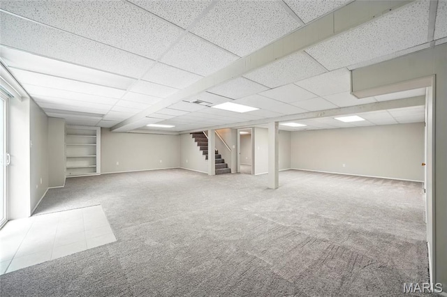 basement with carpet, stairway, built in features, a drop ceiling, and baseboards