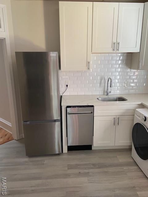 6330 Clayton Ave, Saint Louis, MO 63139 - kitchen with appliances with stainless steel finishes, a sink, washer / dryer, white cabinetry, and light countertops