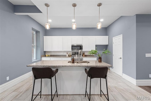 3244 Michigan Ave, Saint Louis, MO 63118 - kitchen featuring stainless steel microwave, a sink, baseboards, a breakfast bar area, and white cabinetry