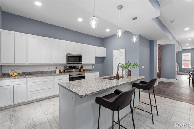 3244 Michigan Ave, Saint Louis, MO 63118 - kitchen with stainless steel appliances, a sink, white cabinets, light stone countertops, and an island with sink