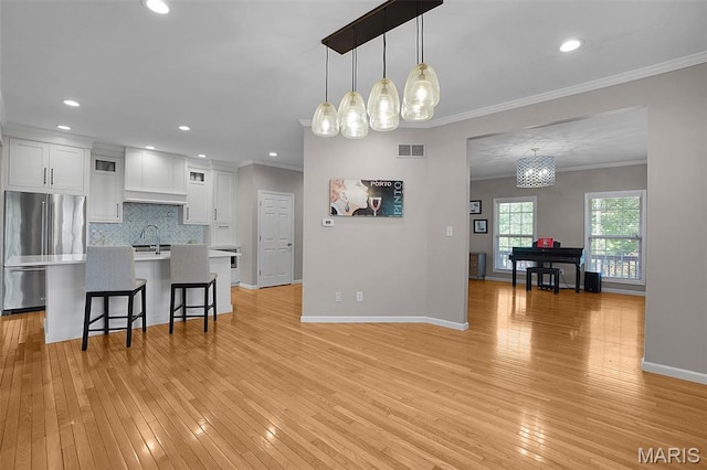 385 E Clinton Pl, Saint Louis, MO 63122 - kitchen with stainless steel fridge, white cabinets, a breakfast bar, ornamental molding, and light wood-style floors