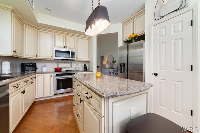 kitchen with cream cabinets, appliances with stainless steel finishes, backsplash, and a center island