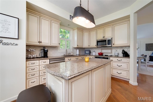 kitchen featuring cream cabinetry, stainless steel microwave, tasteful backsplash, and light wood-style floors