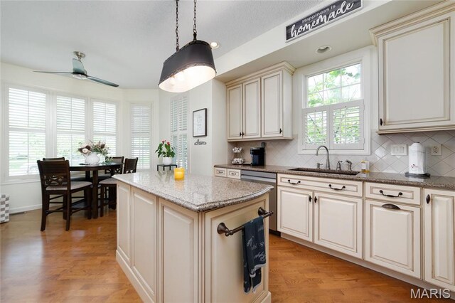kitchen featuring a sink, decorative backsplash, ceiling fan, a center island, and light wood-style floors