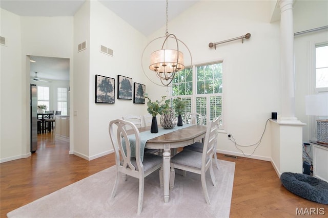 dining area featuring wood finished floors, a chandelier, high vaulted ceiling, baseboards, and ornate columns